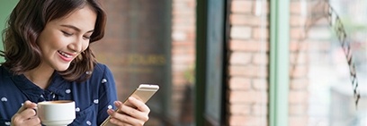 Woman smiling at her phone and holding white coffee mug