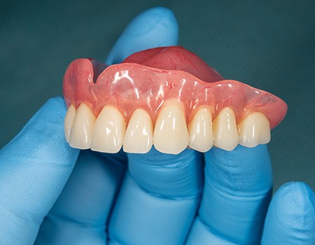 A senior woman holding a denture away from her mouth