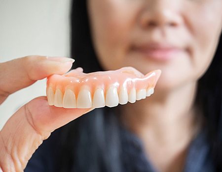 A woman holding upper dentures between her fingers