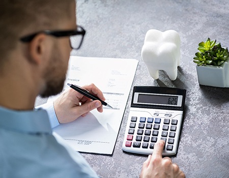 Man using calculator with tooth sitting nearby