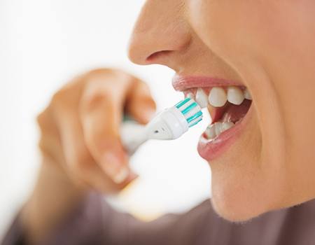Close-up of woman brushing her teeth with an electric toothbrush