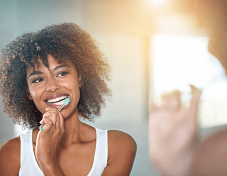 a woman brushing her teeth to avoid dental emergencies