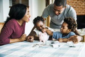 family sitting at a table and placing money in a piggy bank