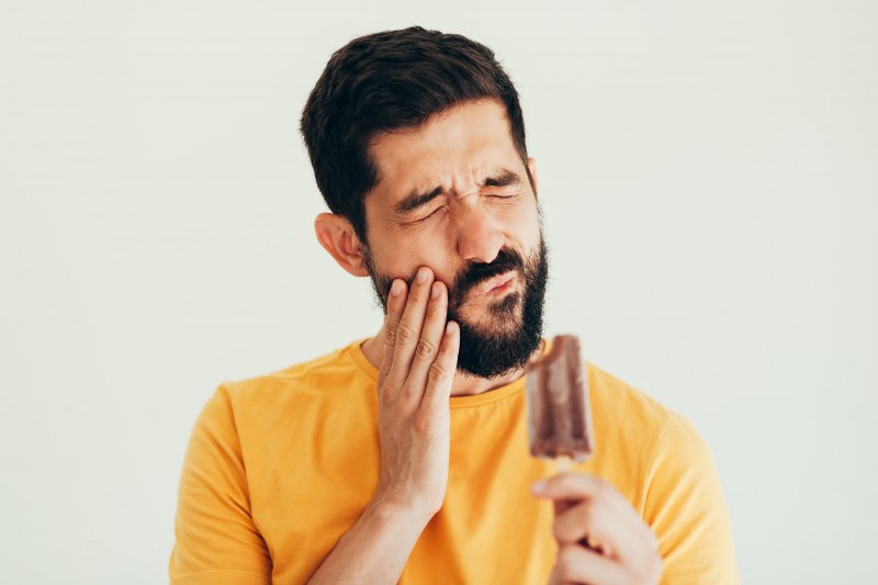 Closeup of man experiencing tooth sensitivity while eating a popsicle