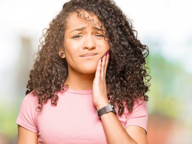 person with tooth pain holding their cheek