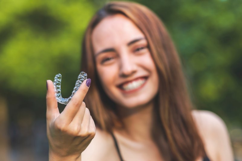 woman smiling and holding Invisalign tray in Willow Grove