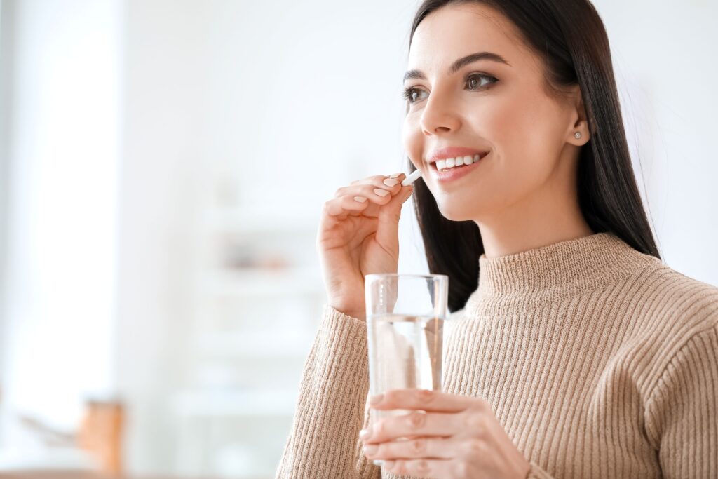 Woman in brown sweater about to swallow pill with glass of water